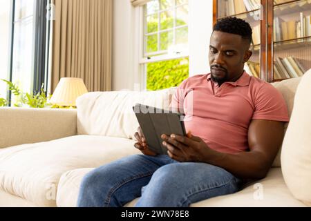 Homme afro-américain dans une chemise rose est concentré sur une tablette Banque D'Images