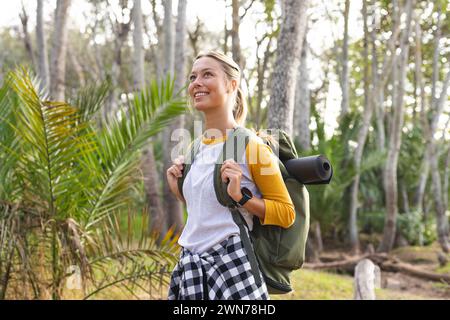 Une jeune femme aux cheveux blonds sourit en randonnée dans une forêt lors d'une randonnée Banque D'Images