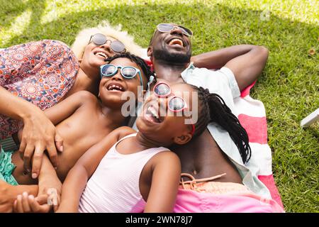 La famille afro-américaine profite d'une journée ensoleillée à l'extérieur, allongée sur l'herbe avec des sourires lumineux Banque D'Images