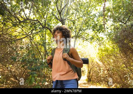 Jeune femme biraciale avec les cheveux bouclés aime une randonnée dans une forêt luxuriante Banque D'Images