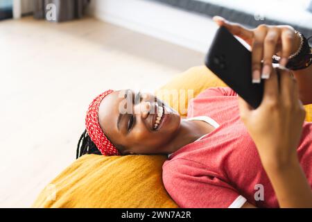 Jeune femme afro-américaine prend un selfie allongée sur un canapé jaune Banque D'Images