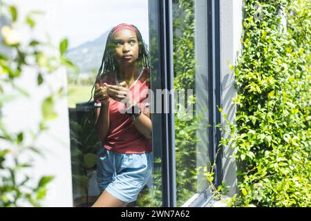 Une jeune femme afro-américaine regarde soigneusement à travers une fenêtre avec un espace de copie Banque D'Images