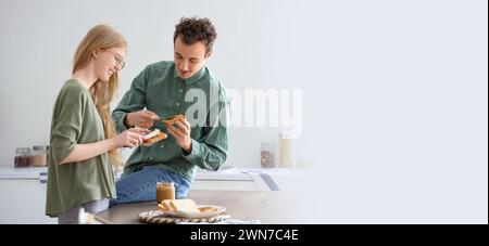 Jeune femme et homme étalant du beurre de noix sur des toasts dans la cuisine. Bannière pour la conception Banque D'Images