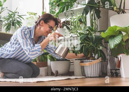 Une jeune femme aime prendre soin des fleurs. Arroser les plantes d'intérieur et les admirer. Banque D'Images