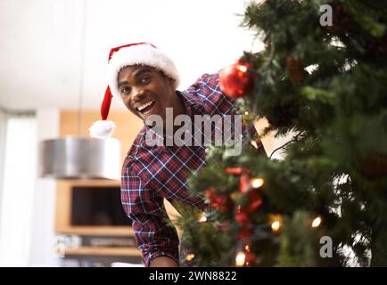 Portrait, énergie et homme noir avec arbre de Noël dans le salon de la maison pour la décoration ou les vacances. Sourire, célébration en décembre et heureux jeune Banque D'Images