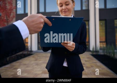 Joyeuse dame écrivant quelque chose sur le presse-papiers tenu par la main de l'homme Banque D'Images