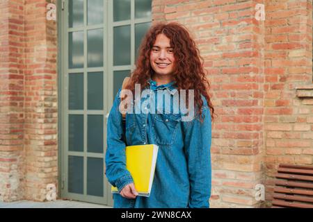 Portrait individuel d'un étudiant optimiste debout et regardant la caméra sur le campus universitaire. Adolescent positif tenant un cahier au lycée. Jeune adulte regardant devant l'académie. Photo de haute qualité Banque D'Images