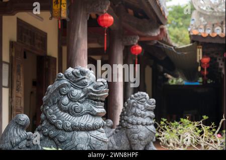 Gros plan sculpture du gardien du lion au temple bouddhiste sur le Marbel Mountian, au centre du Vietnam. Il y a des lanternes rouges suspendues à la structure Banque D'Images