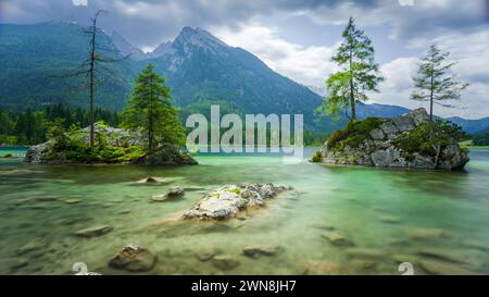 Lac Hintersee près de Ramsau, Berchtesgaden, Bavière, Allemagne. Célèbre vue d'arbres sur des rochers entourés d'eau lisse. Montagnes en arrière-plan. Banque D'Images