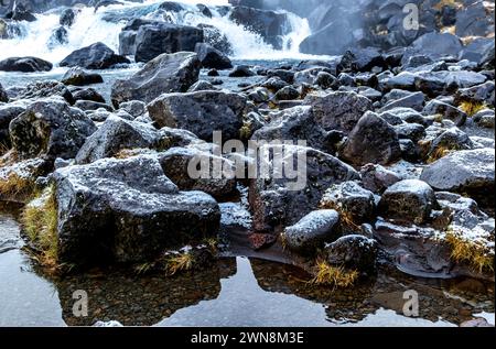 Eau mousseuse rapide coulant à travers des pierres rugueuses érodées et de croissance d'herbe dans un terrain montagneux en plein soleil. Parc national de Thingvellir, Islande Banque D'Images