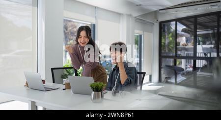 Deux entreprises asiatiques lève les mains vers le haut se réjouit dans l'augmentation des profits dans les affaires. Femme d'affaires et homme reçoit de bonnes nouvelles en ligne, l'élevant Banque D'Images