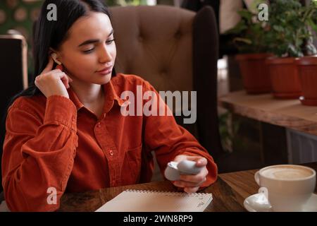 Le temps d'écouter de la musique et de se détendre concept. Mignonne jeune femme sort les mini écouteurs bluetooth sans fil modernes d'un étui de charge et les mettre dans l'oreille Banque D'Images