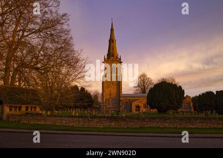 Lever de soleil à l'église St Peter dans le village de Sharnbrook, Bedfordshire, Angleterre, Royaume-Uni. Le cimetière avec son lychgate et son mur de pierre sont également visibles Banque D'Images