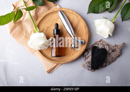 Composition d'auto-soin avec sérum facial, gua Sha, rouleau facial. Arrangement holistique de beauté avec des roses. Banque D'Images