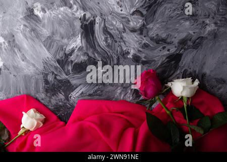 Roses vibrantes couchées sur un fond gris abstrait texturé drapé de rose. Banque D'Images
