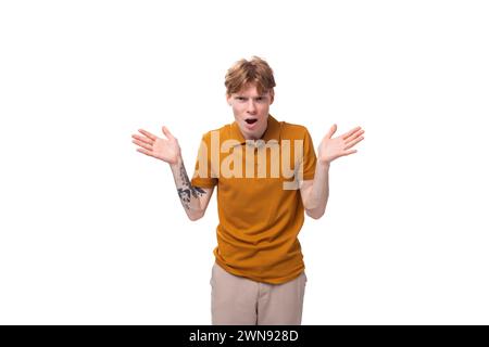 jeune étudiant à la mode avec les cheveux rouges courts habillé d'un t-shirt jaune est activement gestuant Banque D'Images