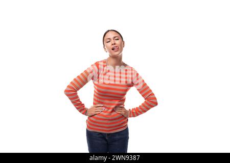 une jeune femme caucasienne agréable aux cheveux noirs est habillée d'un pull rayé orange grimacant Banque D'Images
