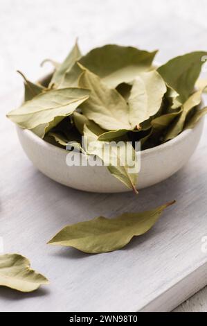 Feuilles de laurier séchées dans un bol sur fond rustique, concept d'épices et d'herbes (Laurus nobilis) Banque D'Images