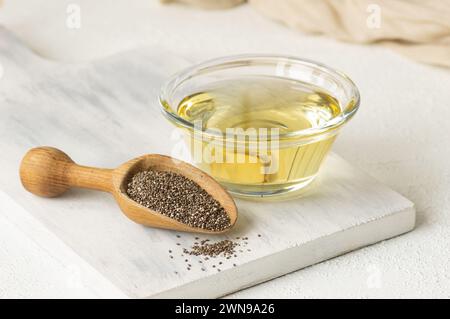 Bouteille en verre d'huile de chia avec des graines de chia ( Salvia hispanica ) en pelle en bois sur fond rustique Banque D'Images