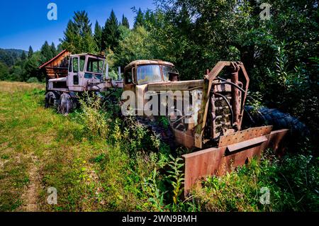 Vieilles machines détruites, souffleuse à neige abandonnée et machine dans les buissons. Véhicules lourds rouillés, inutilisés dans une forêt de montagne. Bieszczady, ensoleillé, été Banque D'Images