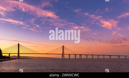 Un coucher de soleil serein avec un ciel rose et orange vif sur un pont et l'eau calme, Vasco Da Gama Bridge, Lisbonne Banque D'Images