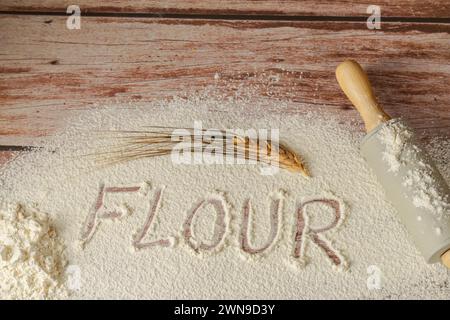 Farine tamisée sur une table en bois avec le mot farine écrit dessus, à côté d'une épi de blé et d'un rouleau à pâtisserie, fond en bois et espace de copie Banque D'Images
