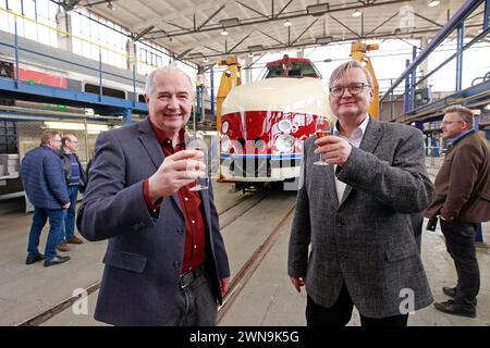 01 mars 2024, Saxe-Anhalt, Halberstadt : Mario Lieb de SVT Görlitz (à droite) et Ronald Krahl de Verkehrs industrie SYSTEME vis Halberstadt boivent une coupe de champagne au cours de la rénovation de la SVT. Le train de prestige SVT du GDR est lentement posé sur le châssis à l'aide d'une plate-forme élévatrice. Après cette étape, la rénovation de la SVT peut se poursuivre. Sous les yeux vigilants de nombreux invités, la voiture à moteur VT 18.16.10 a été élevée à environ 2,60 mètres dans le dépôt ferroviaire vis Halberstadt à l'aide de quatre vérins de levage, puis les bogies ont été positionnés exactement sous le véhicule. Enfin Banque D'Images