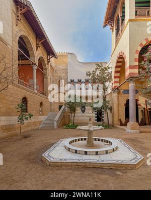 La cour sereine met en valeur la beauté intemporelle de l'architecture mamelouk avec de grandes arches et des pierres avec escalier accueillant menant à un balcon orné. Une fontaine de marbre classique se trouve au centre Banque D'Images