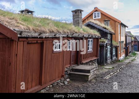 Des cabanes rustiques en bois avec des toits en gazon à Roros mènent le regard sur un chemin de gravier, mettant en valeur le patrimoine de cette ville minière historique norvégienne Banque D'Images