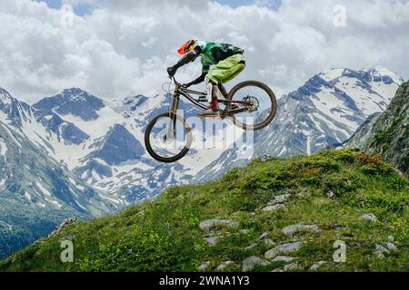Le VTT a sauté, volant en plein air sur fond de sommets enneigés et de verdure luxuriante. compétition de descente Banque D'Images