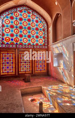 Le vitrail orné projette des éclaboussures de lumière colorées sur le mur et le sol du pavillon. Jardin de Dowlatabad, Yazd, Iran. Banque D'Images