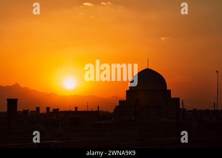 Silhouette d'un bâtiment traditionnel en forme de dôme contre le coucher du soleil et le coucher du soleil orange ciel. Yazd, Iran. Banque D'Images