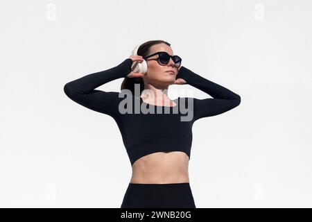 Femme sportive tenant une paire d'écouteurs sur sa tête à l'extérieur contre un mur blanc. Préparation à l'exercice et à l'entraînement Banque D'Images