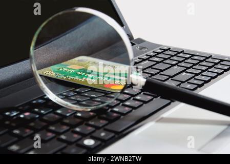 Une loupe en verre repose sur le clavier avec une carte bancaire dans un lieu de travail confortable. Le concept de recherche et de paiement sur Internet. Banque D'Images