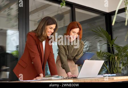 Deux partenaires féminins professionnels souriants travaillant au bureau regardant un ordinateur portable. Banque D'Images