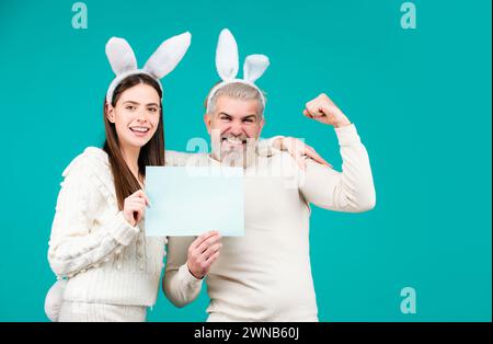 Le couple de Pâques vêtu de costume tenant un tableau blanc vierge pour votre texte. Couple de lapin de Pâques isolé sur fond bleu. Banque D'Images