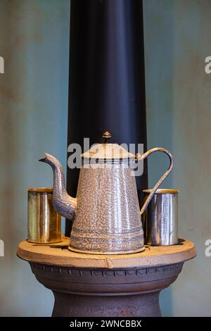 Canette de café et tasses en étain reposant sur un poêle de chauffage au charbon traditionnel Banque D'Images