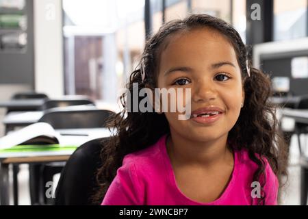 Fille biraciale aux cheveux bouclés souriant dans un cadre de classe d'école Banque D'Images