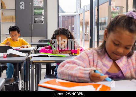 Un garçon afro-américain et deux filles biraciales se sont concentrés sur leur travail scolaire dans une salle de classe Banque D'Images