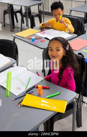 Garçon afro-américain et fille biraciale sont concentrés sur leur travail scolaire dans une classe d'école Banque D'Images