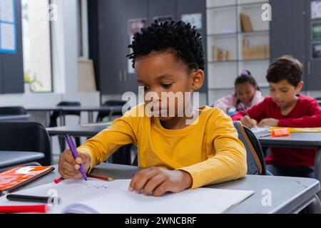 Garçon afro-américain concentré sur le dessin avec un marqueur violet dans une salle de classe d'école Banque D'Images