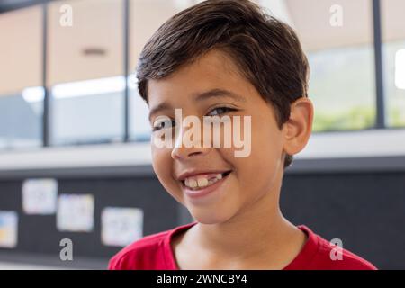 Garçon biracial avec un sourire éclatant, portant une chemise rouge dans une classe d'école Banque D'Images