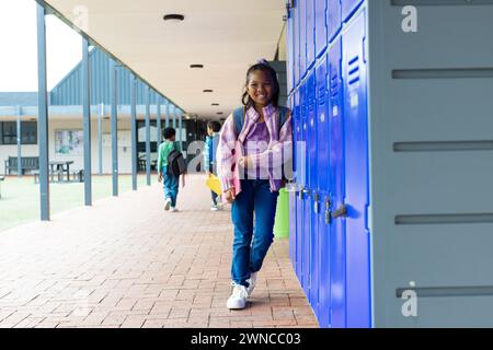 Fille biraciale avec un sourire lumineux se tient par des casiers d'école bleus, avec espace de copie Banque D'Images