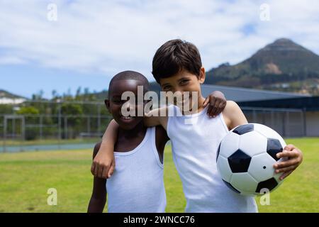 Garçon biracial et garçon afro-américain sourire, tenant un ballon de football à l'école Banque D'Images