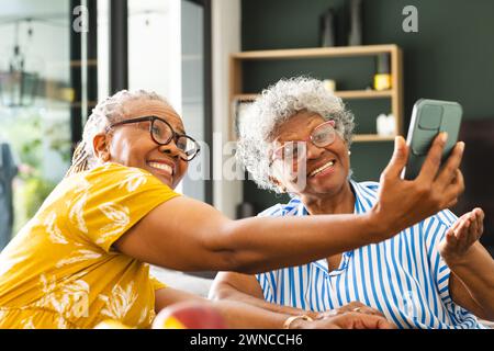 Femme afro-américaine senior et femme biraciale senior sourient tout en prenant un selfie à la maison Banque D'Images