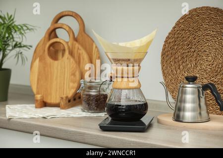 Préparation de café goutte à goutte. Cafetière chemex en verre avec filtre en papier, pot de haricots et bouilloire sur comptoir en bois dans la cuisine Banque D'Images