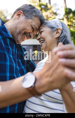 Femme biraciale senior et homme biracial partagent un moment joyeux, embrassant à l'extérieur Banque D'Images