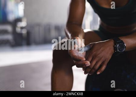 Gros plan d'une femme biraciale forte et en forme enveloppant sa main avec du ruban adhésif athlétique, avec espace de copie Banque D'Images