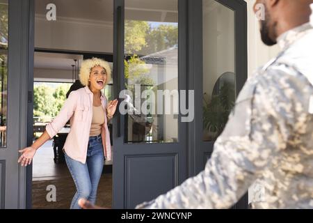 Une jeune femme biraciale excitée accueille un soldat afro-américain en uniforme militaire à la porte Banque D'Images