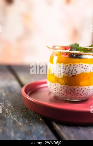 Chia Seed Pudding avec mangue et baies dans un pot en verre sur une assiette rouge Banque D'Images